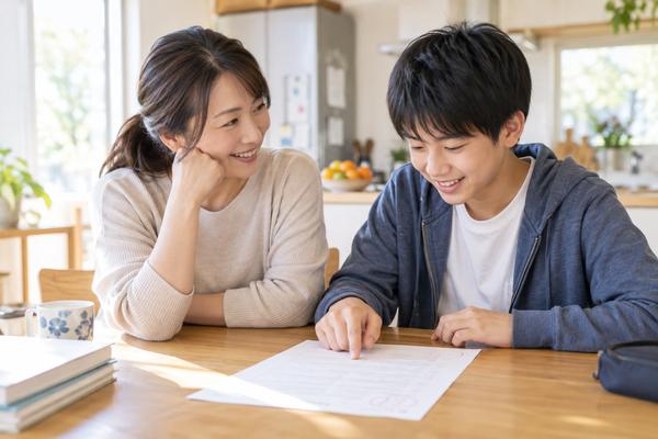 返却された英語の答案を母親と中学生の息子が笑顔で一緒に見ながら、次に直すところを話している様子