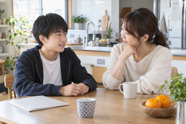 テストを脇に置いたまま、自宅のテーブルで穏やかに話している中学生と保護者