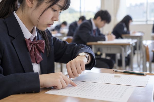 模試の会場で腕時計を確認しながらマークシートを進めている制服の高校生