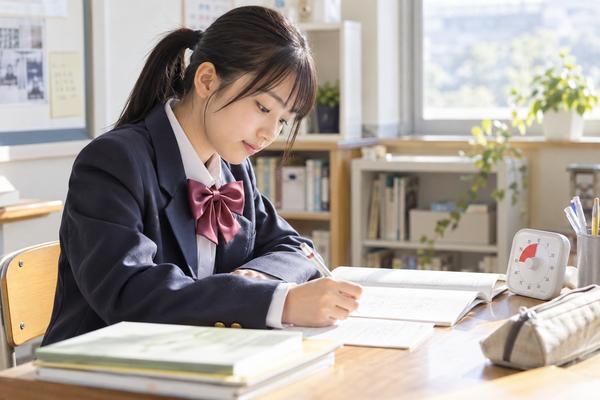 机に置いた時計で時間を測りながら、同じ種類の問題を解き直している制服姿の中学生