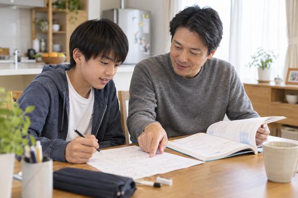 自宅のテーブルで、中学生と保護者が丸付けの済んだ答案と学校ワークを並べて復習している様子