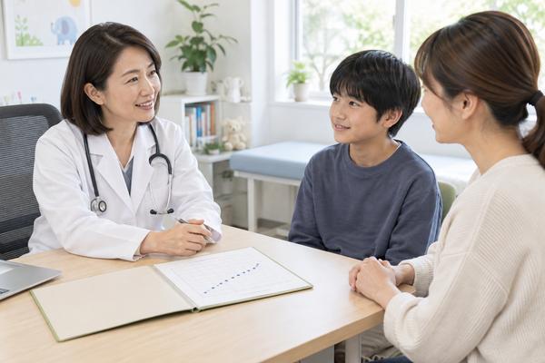 小児科で医師が成長曲線の記録を見せながら、中学生の男子と母親に説明している様子