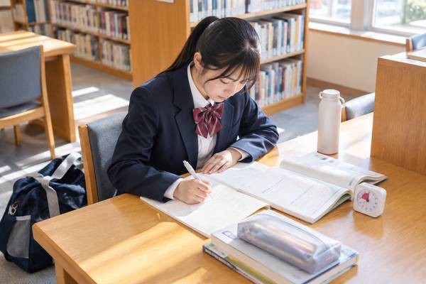 明るい図書室で、制服姿の中学生がタイマーを置き、問題集を開いて過去問の解き直しに取り組んでいる様子