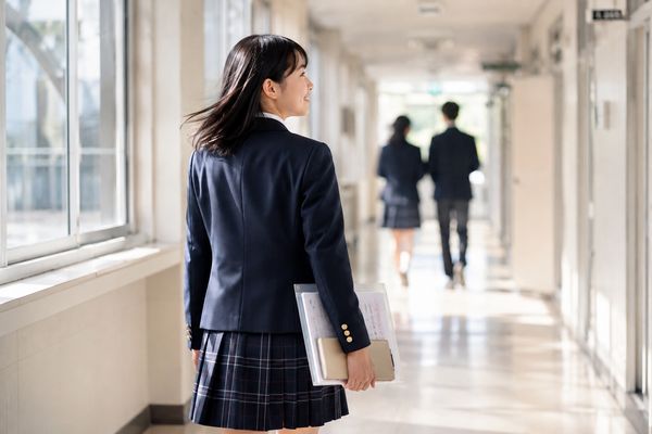 返却答案をファイルに入れ、明るい校舎の廊下を歩く制服の高校生