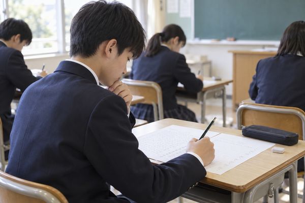 定期テスト中の教室で、中1の男子生徒が鉛筆を止めて答案全体を見渡し見直しをしている様子