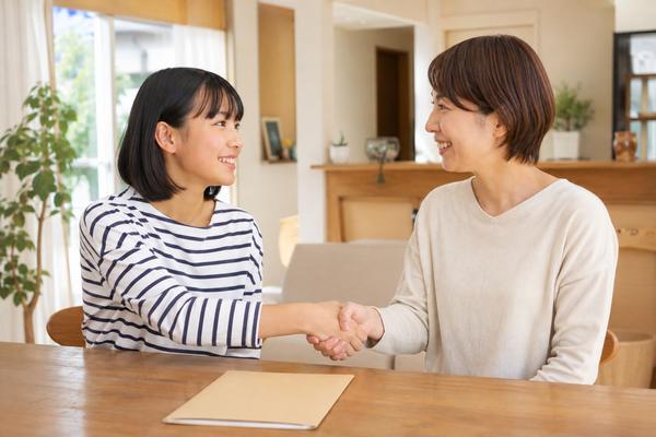 自宅のテーブルで通知表を前に、私服の中学生と保護者が笑顔で握手し次の作戦を決めた様子