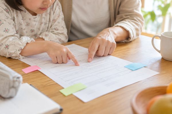 ダイニングテーブルで学校からの案内を指でたどり、三色の付箋を貼って確認している親子の手元