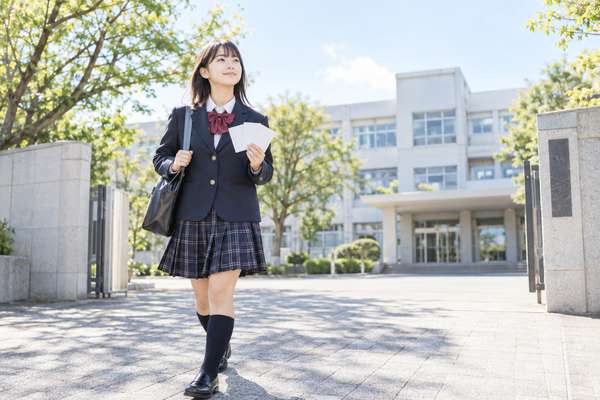 晴れた日に校門の前で笑顔を見せる制服姿の中学生