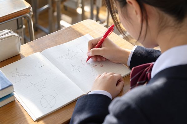 教室の机で、制服姿の中学生が赤ペンを持ち、ノートの間違いを一問ずつ直している手元の様子