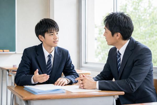 放課後の教室で答案を前に先生へ評価の理由を具体的に質問する男子中学生