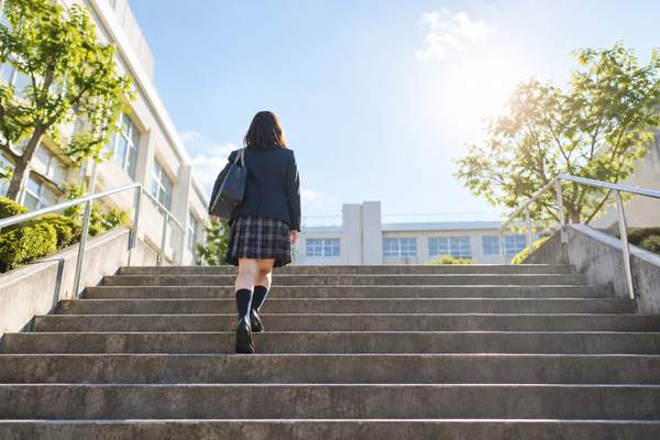 校舎へ続く明るい階段を一段ずつ上っていく制服姿の中学生
