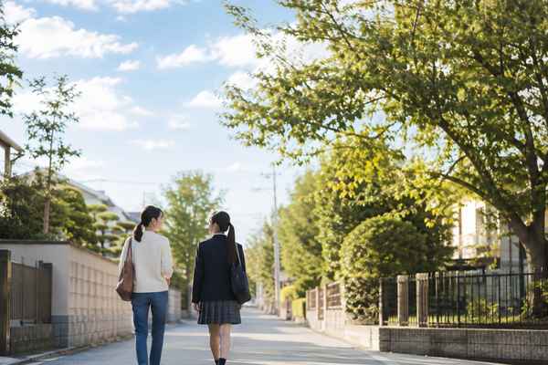 夕方の明るい住宅街を、制服姿の中3の生徒と保護者が並んで歩いて帰る後ろ姿