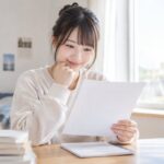 明るい窓辺の机で、浪人生の女性が模試の結果を1枚手に取り、落ち着いた表情で自分の数字を確かめている様子