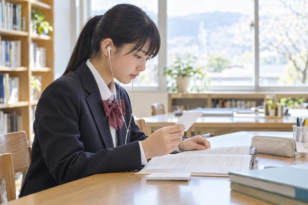イヤホンで英語を聞きながら、問題冊子とメモを見比べる制服の中学生