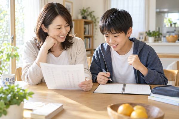中学1年生の通知表を食卓で一緒に見ながら、次の学期の話をしている保護者と男子生徒