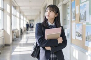 明るい校舎の廊下で、進路掲示の前に立ち止まって考える制服姿の高校3年生