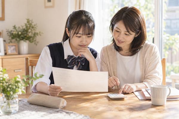 返却されたテストの答案を電卓で計算しながら母親と一緒に見直す中学生