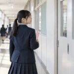 明るい校舎の廊下でファイルを抱え教室へ向かう制服の中学生