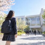 桜の咲く高校の正門から校舎へ向かって歩き出す新入生