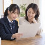自宅のテーブルで通知表を一緒に見ている制服の生徒と保護者