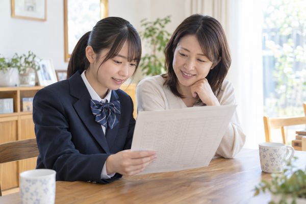 自宅のテーブルで通知表を一緒に見ている制服の生徒と保護者