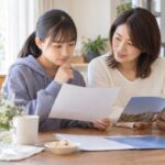 通知表と高校の資料を広げ、成績ランクが何を指すのかを保護者と一緒に確かめている中学生
