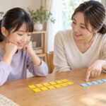 自宅のテーブルで、黄色と青のタイルを並べながら割合の意味を一緒に考える小学生と母親