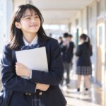 返却されたテストの答案を胸の前に持ち、校舎の廊下でほっとした表情を見せる制服の中学生