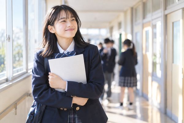 返却されたテストの答案を胸の前に持ち、校舎の廊下でほっとした表情を見せる制服の中学生