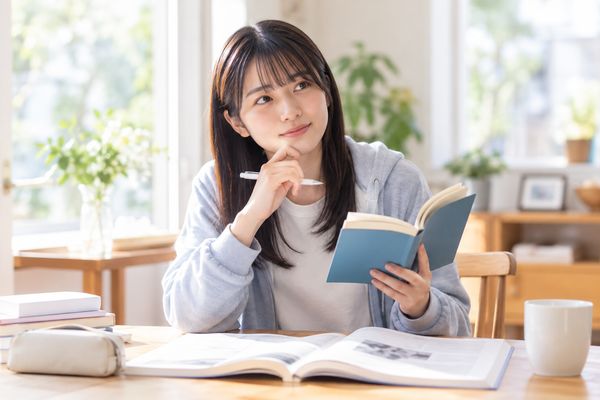 英語の長文を前に、単語帳を手にしたまま意味を思い出そうと考え込んでいる高校生