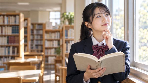 明るい図書室の窓辺で、漢文の参考書を開いて考えている制服姿の高校生
