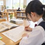 明るい学校図書室で、漢文の練習プリントを広げて読む順番を書き込んでいる制服姿の高校生