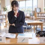 学校図書室で、本・鉛筆・ヘッドホンのアイコンが付いた3種類の英語テスト教材を見比べる制服の中学生