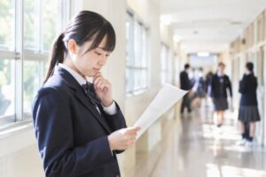 明るい校舎の廊下で、返却された定期テストの答案を手に持ち、成績を考え込む制服の中学生