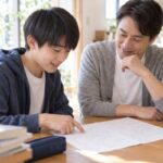 日当たりのよいダイニングで、中学生の息子と父親が返却された5教科のテストを一緒に見ながら笑顔で話している様子