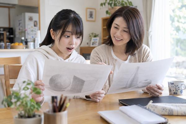 自宅のテーブルで、中学生の娘と母親が美術の授業で描いたデッサンを並べて見ている様子
