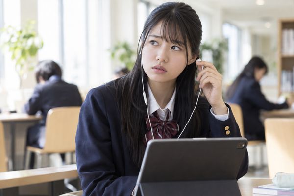 リスニング音声を途中で止め、片耳のイヤホンを外して考え込む制服姿の高校生