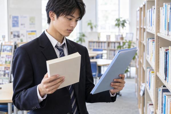 進路資料室で受験参考書と学校の科目ファイルを見比べる制服姿の高校3年生
