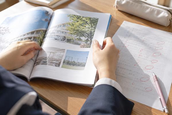 赤で丸をつけられた答案と学校案内を机に広げて見ている高校生