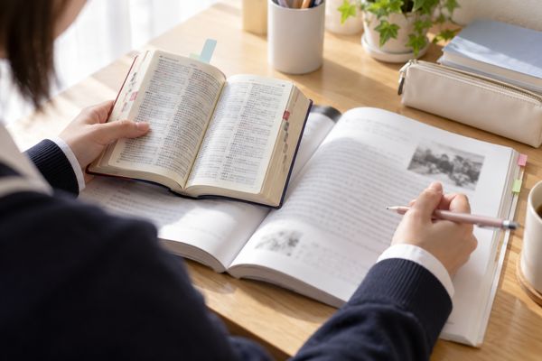 机の上で単語帳と英語の長文を並べ、交互に指でたどっている高校生の手元