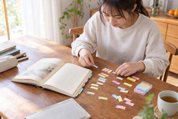 開いた参考書の横で、ばらばらの付箋を並べ替えて句法を整理している高校生