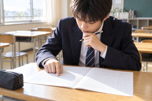 制服姿の高校生が放課後の教室で、本文に指を当てながらマーク式問題の選択肢を見比べている様子