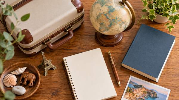 海外経験の違いを表すスーツケースと地球儀、英語の本と旅の思い出の品が並ぶ木の机