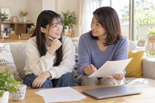 自宅のリビングで大学の資料を見ながら入試方式を母親と相談する高校3年生