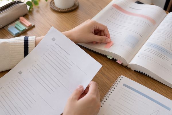 解き終えた過去問の横で教科書の該当ページに付箋を貼り、戻る場所を確かめている高校生の手元
