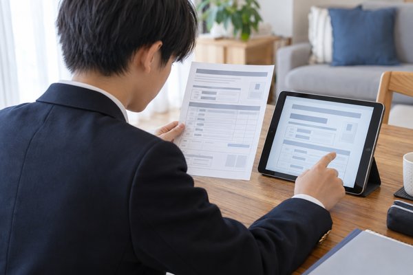 模試の申込内容とタブレットの画面を見くらべて登録情報を確かめる中学3年生