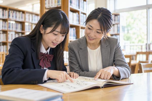 図書室で古典の本文を指さしながら、書き下し文と現代語訳を確かめている生徒と先生