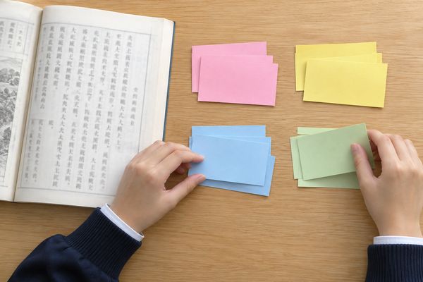 8枚の暗記カードを4色のグループに分ける高校生の手と漢文の本