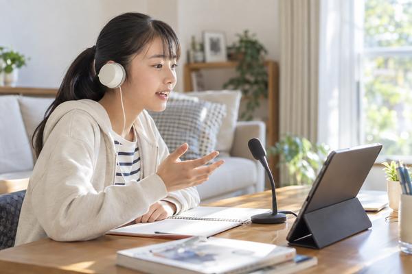 明るい自宅のリビングで、ヘッドホンとマイクに向かって英語を声に出して答える中学生