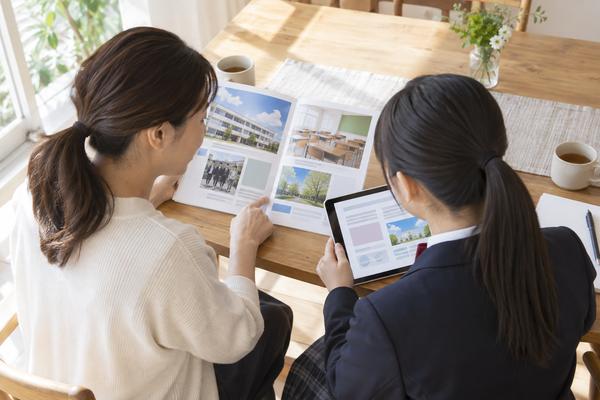自宅のダイニングで、保護者と制服の中学生が志望校の資料を一緒に確認している様子